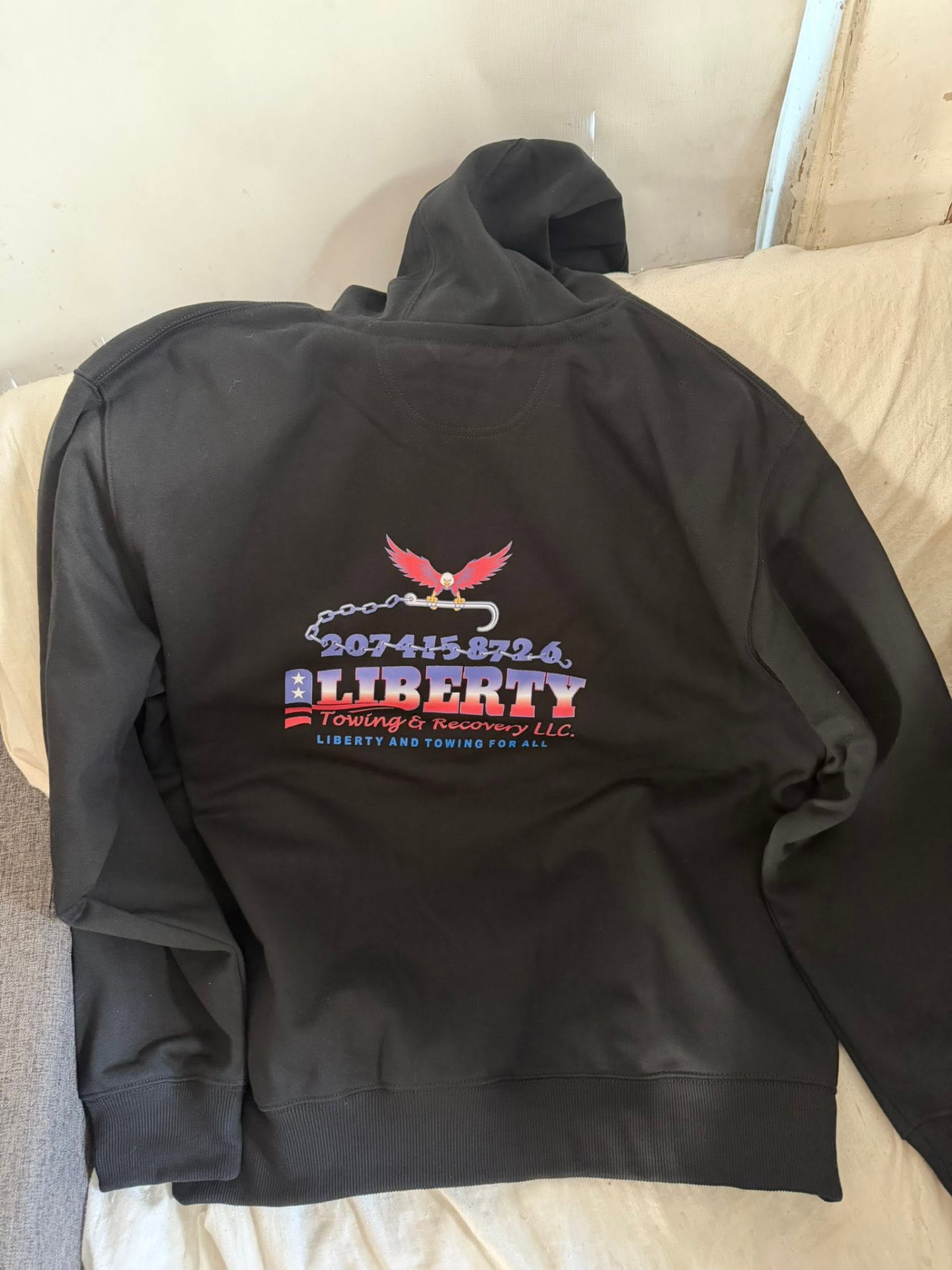 Back of a dark Carhartt hoodie with the Liberty eagle logo and phone number