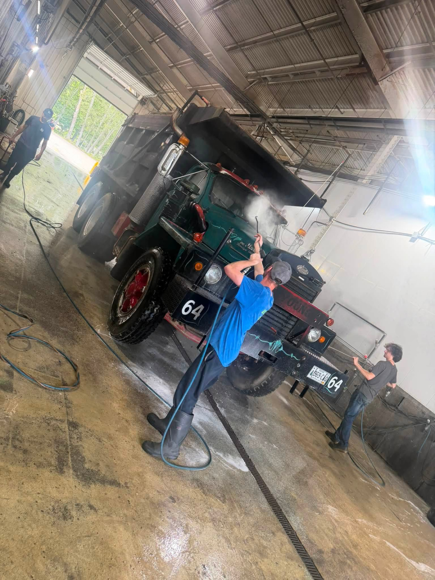 Liberty's crew pressure-washing a vintage green Mack dump truck inside the wash bay