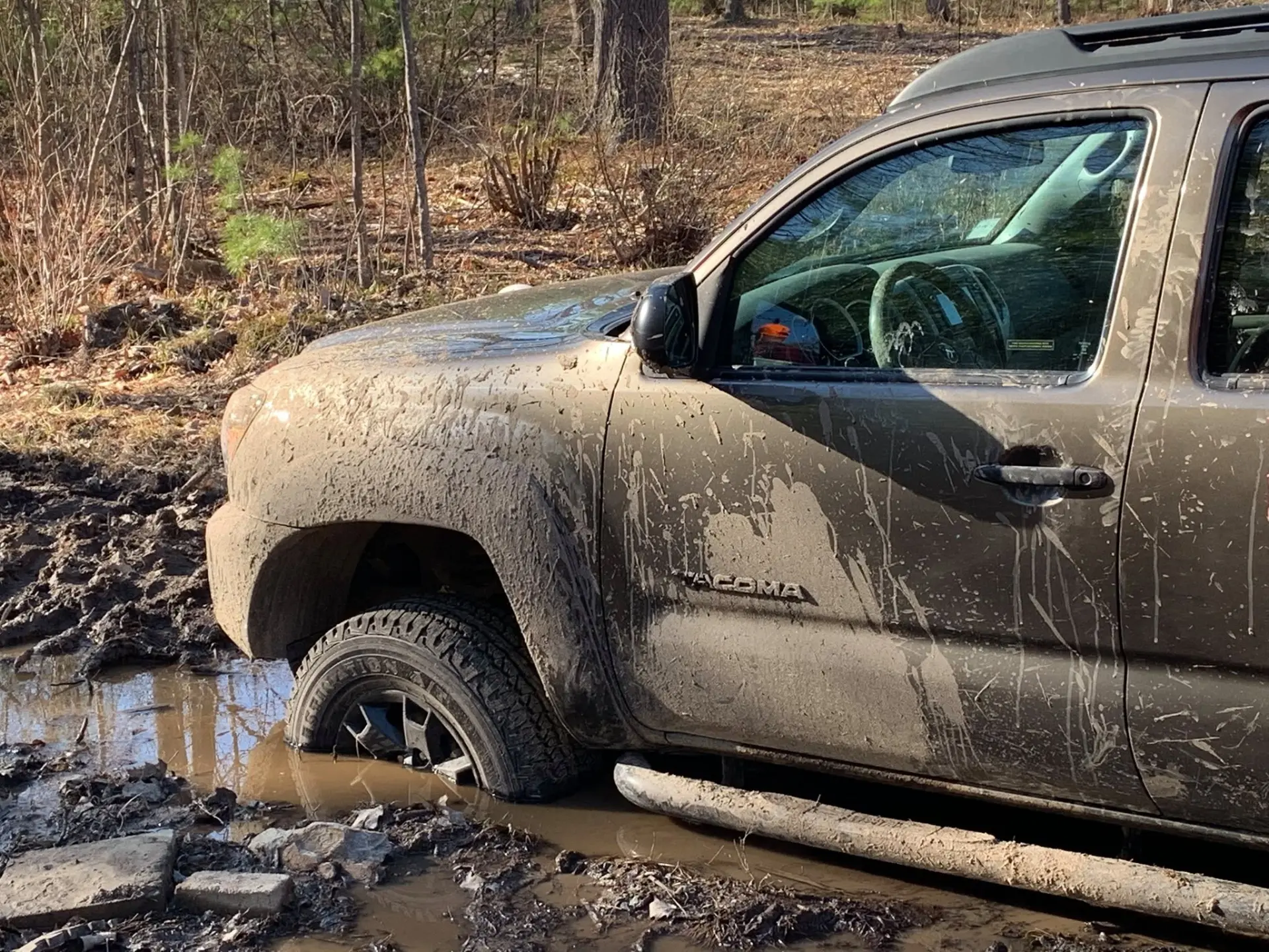 Mud-covered pickup with its front wheel stuck in deep mud in the woods
